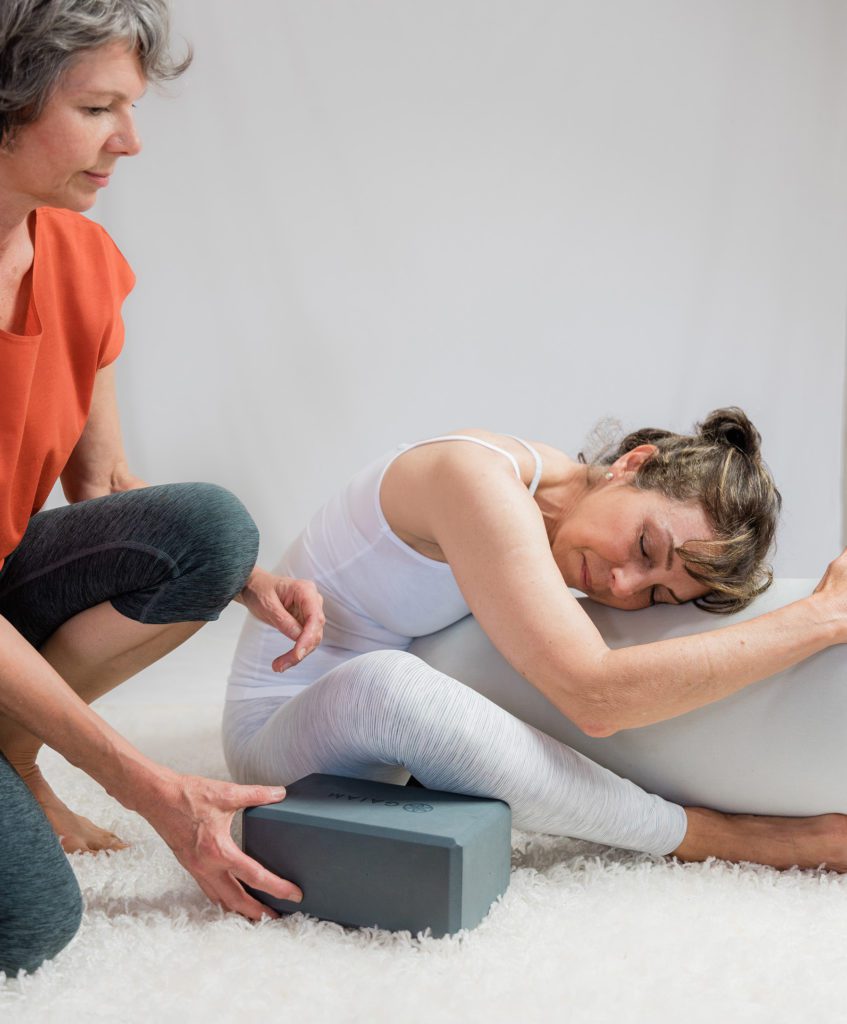Yin Yoga teacher helps student with prop in class