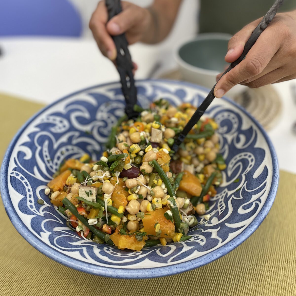 Two hands use wooden salad servers to serve an autumn bounty salad with sweetcorn and butternut squash