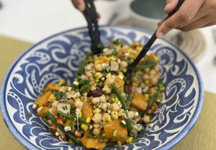 Two hands use wooden salad servers to serve an autumn bounty salad with sweetcorn and butternut squash